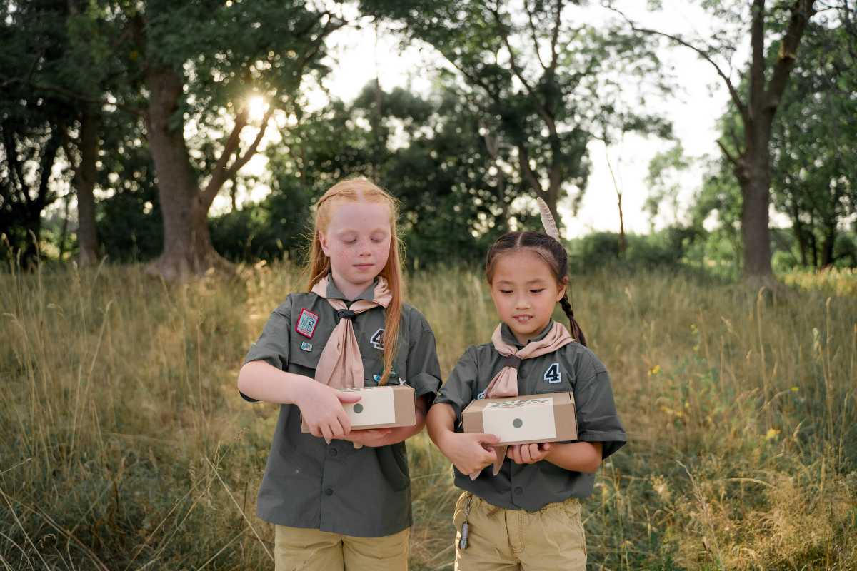 Girls Scout Looking at the Boxes they're Holding while Standing on Grassy Area